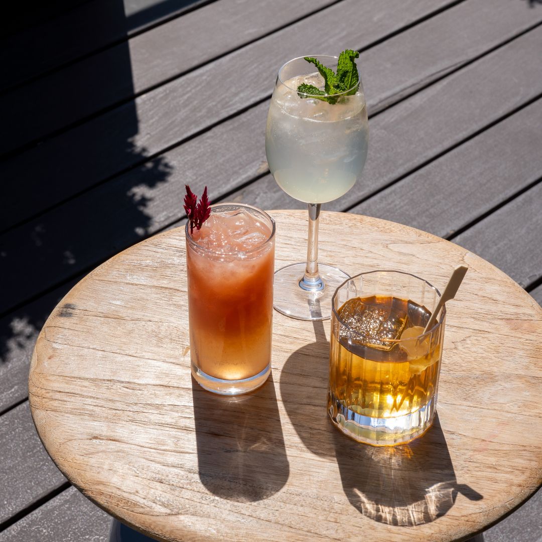 A table with three drinks: a pink cocktail, a clear drink with mint, and a whiskey with ice.